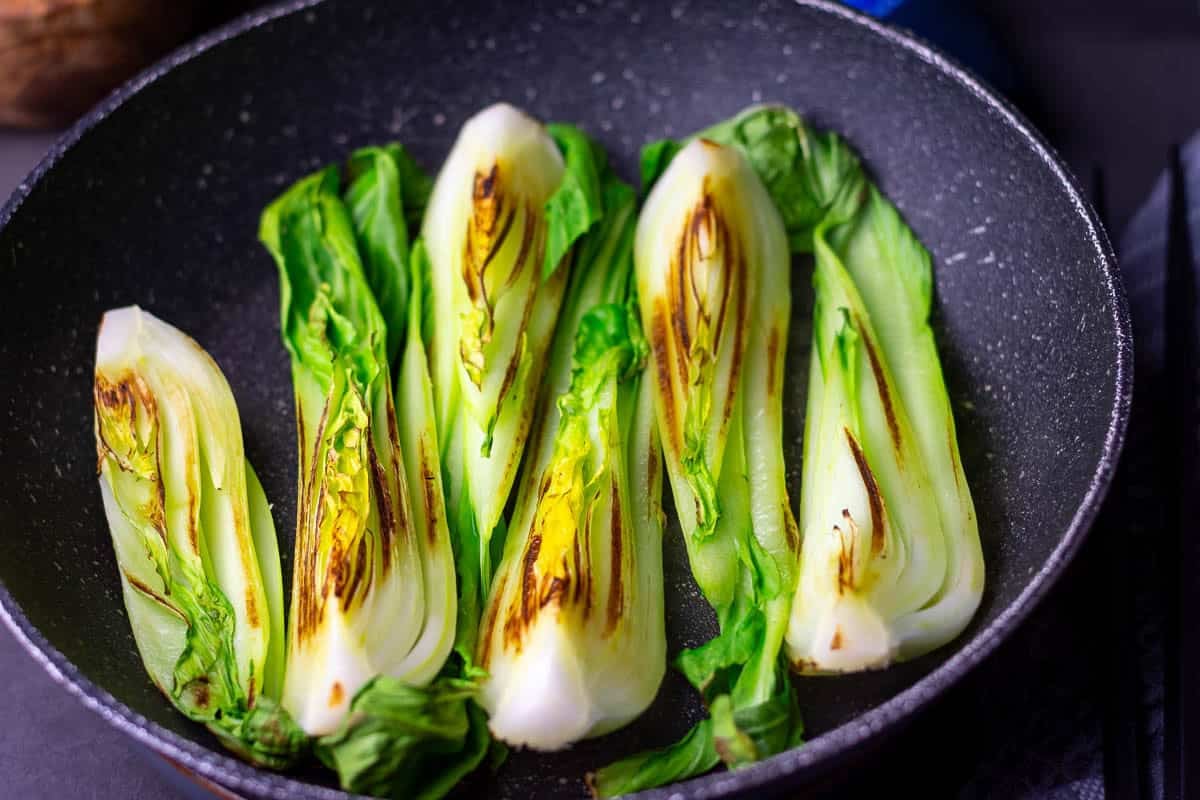 Quartered pak choi charring in a frying pan.