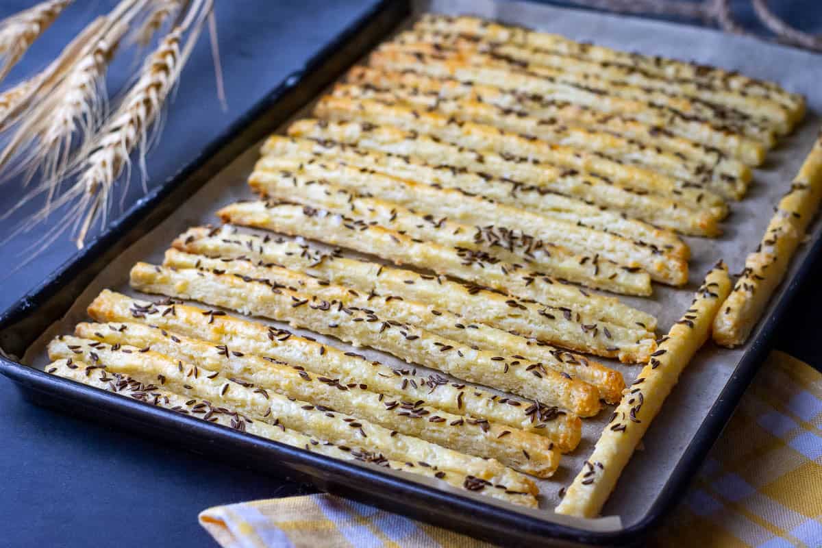 Baked cheese straws cooling on a baking sheet.
