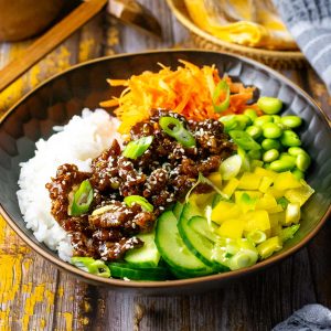 Crispy teriyaki beef rice bowl with pickled carrots and carrots on a wooden table.