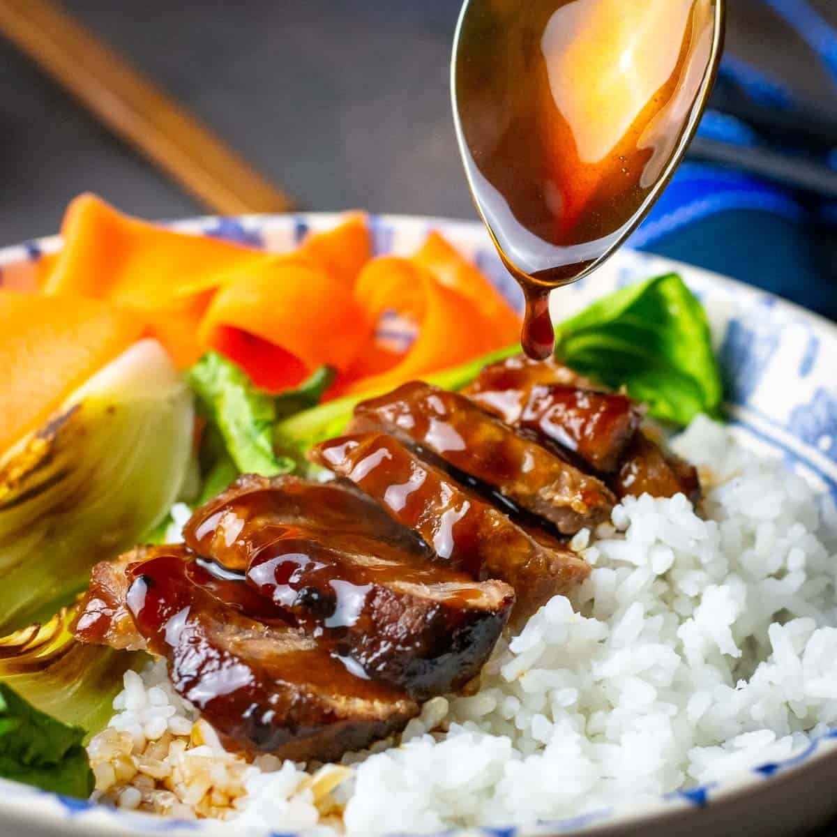 Sliced teriyaki pork tenderloin on a bed of rice being drizzled with extra teriyaki sauce.
