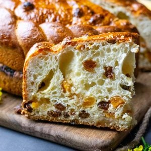 A slice of fruit studded Sourdough Paska (Ukrainian Easter Bread) on a wooden board.