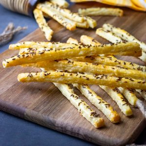 Sourdough discard cheese straws with caraway seeds on top n a wooden board.