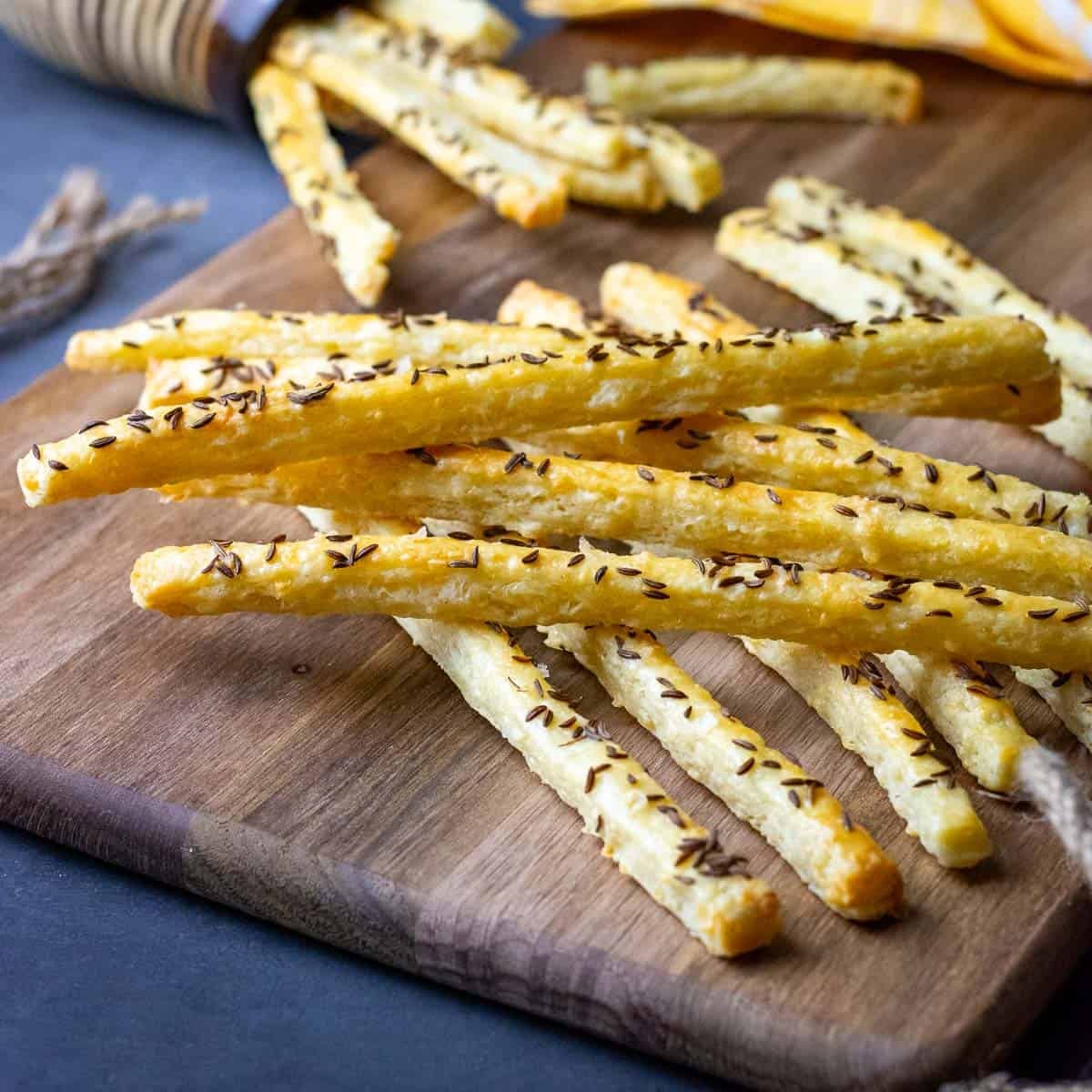 Sourdough discard cheese straws with caraway seeds on top n a wooden board.