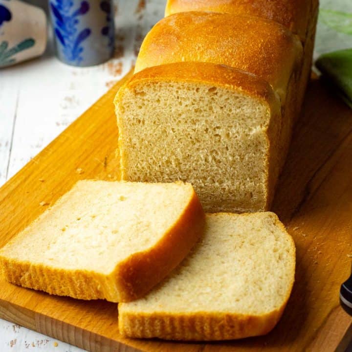 Soft Evaporated Milk Sourdough Sandwich Bread on a wooden board with two slices cut.