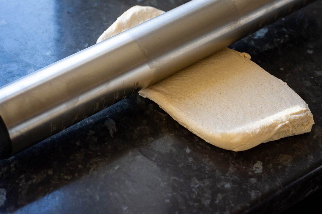 Rolling a piece of sourdough with a stainless steel rolling pin.