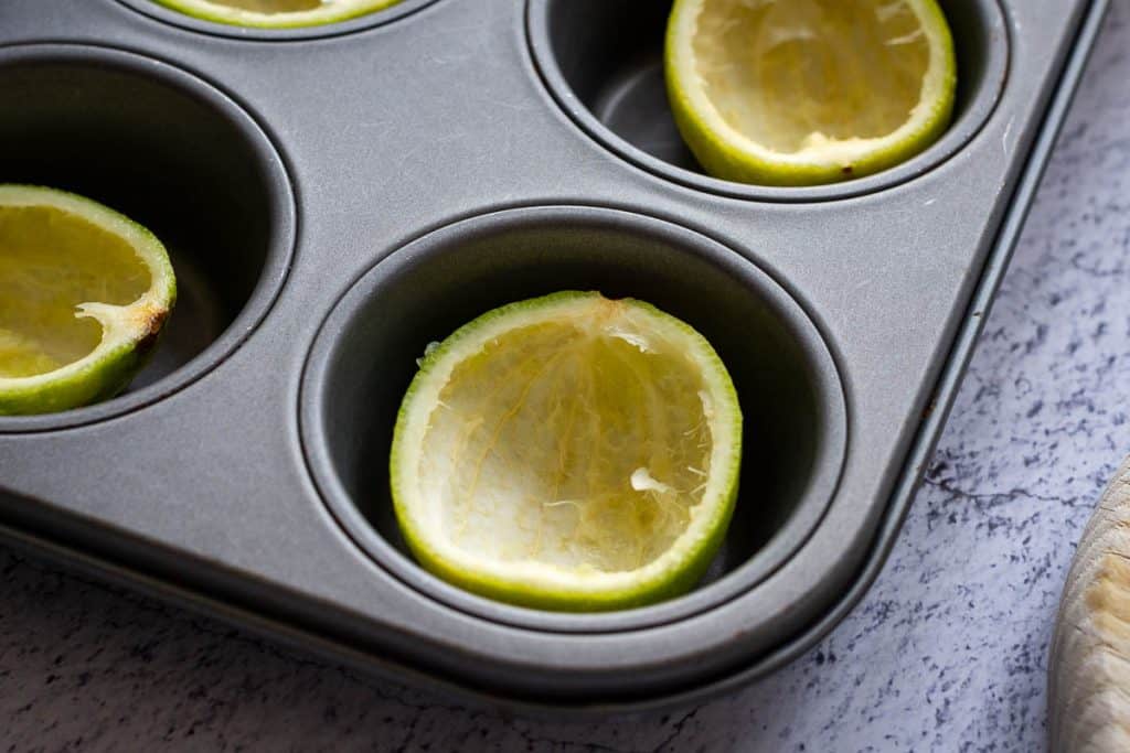 Hollowed lime shells arranged in a muffin pan to keep them steady for filling with lime posset mixture.