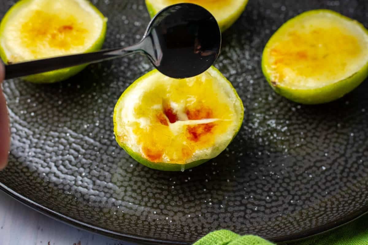 Caramel topping on top of lime posset being broken with the back of a tea spoon.