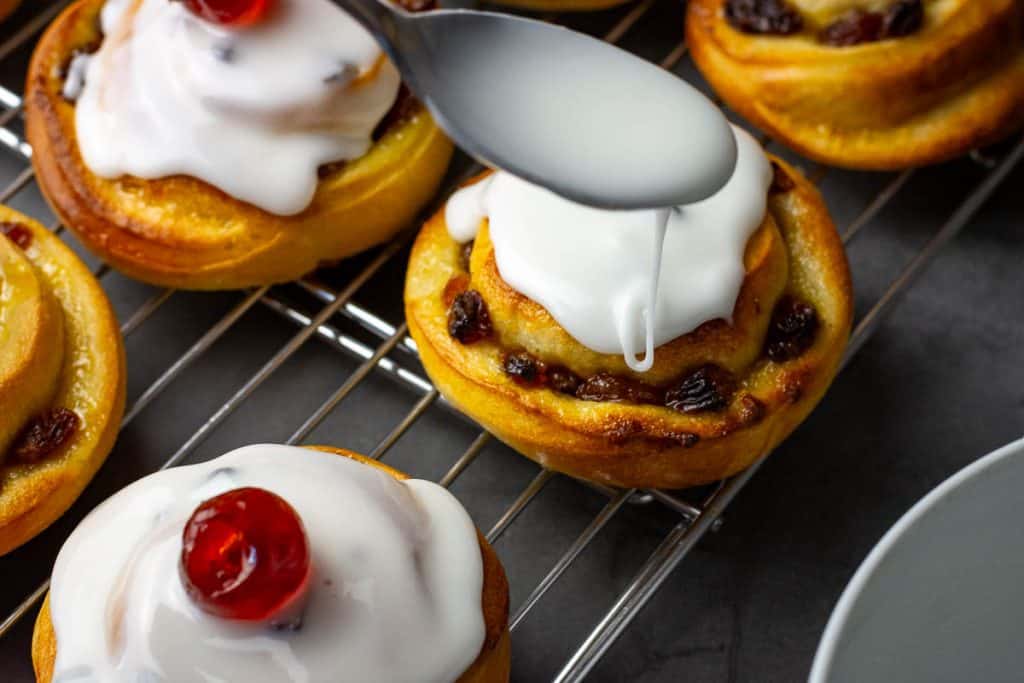 Spreading icing on Sourdough buns with a spoon.