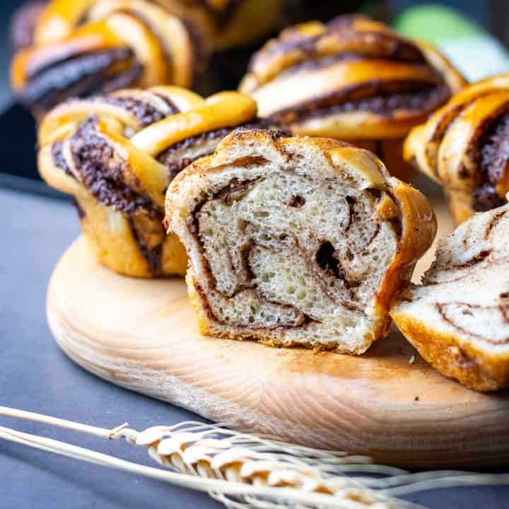 Sourdough chocolate knots on a wooden board with one sourdough chocolate roll cut in half exposing a swirl inside.