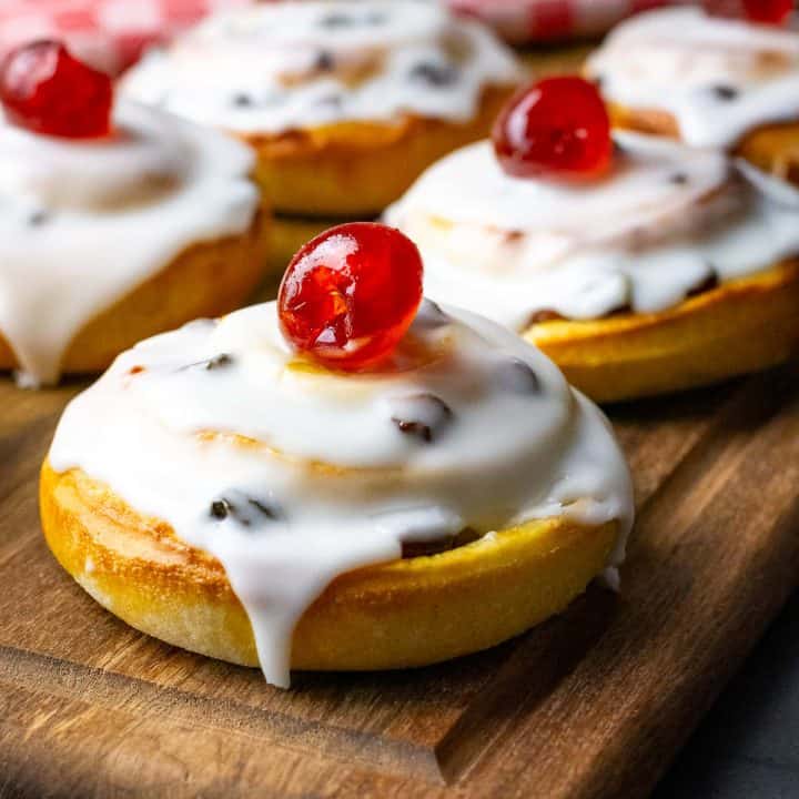 Sourdough Belgian Buns with icing and cherry on top on a wooden board.