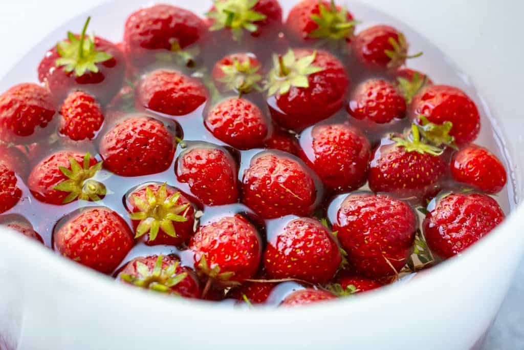 Strawberries being washed in a white bowl.