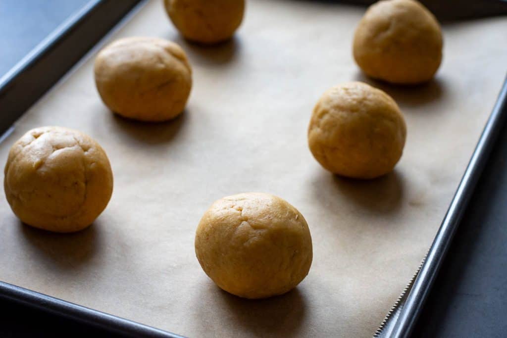 Sourdough sugar cookie dough balls arranged on a parchment paper lined baking sheet.