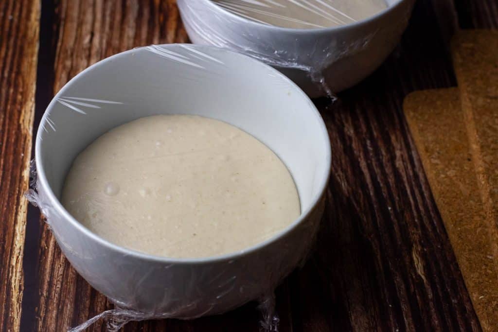 Sourdough pizza dough after ambinet bulk fermentation in two white bowls.
