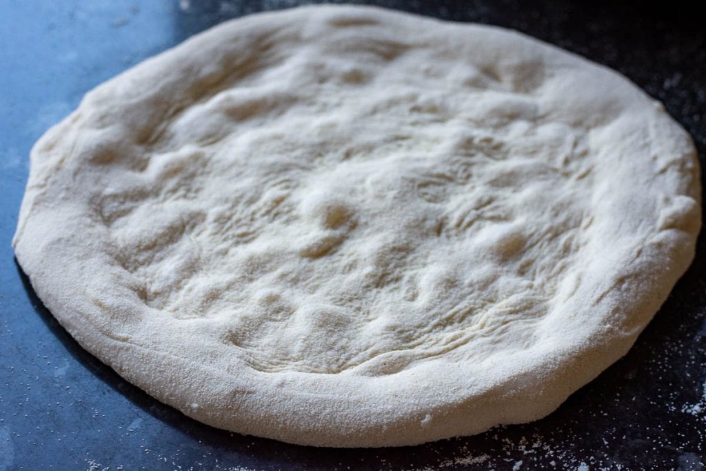 Sourdough pizza crust streatched out on a work top dusted with semolina.