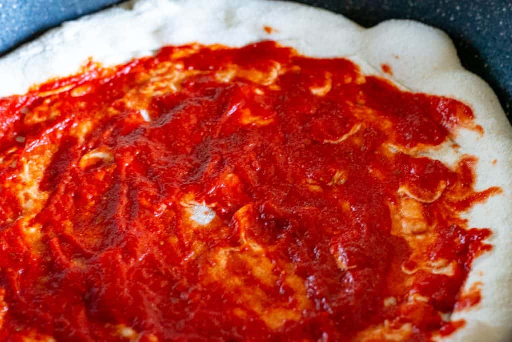 Sourdough pizza dough with tomato sauce spread across it in a large frying pan.