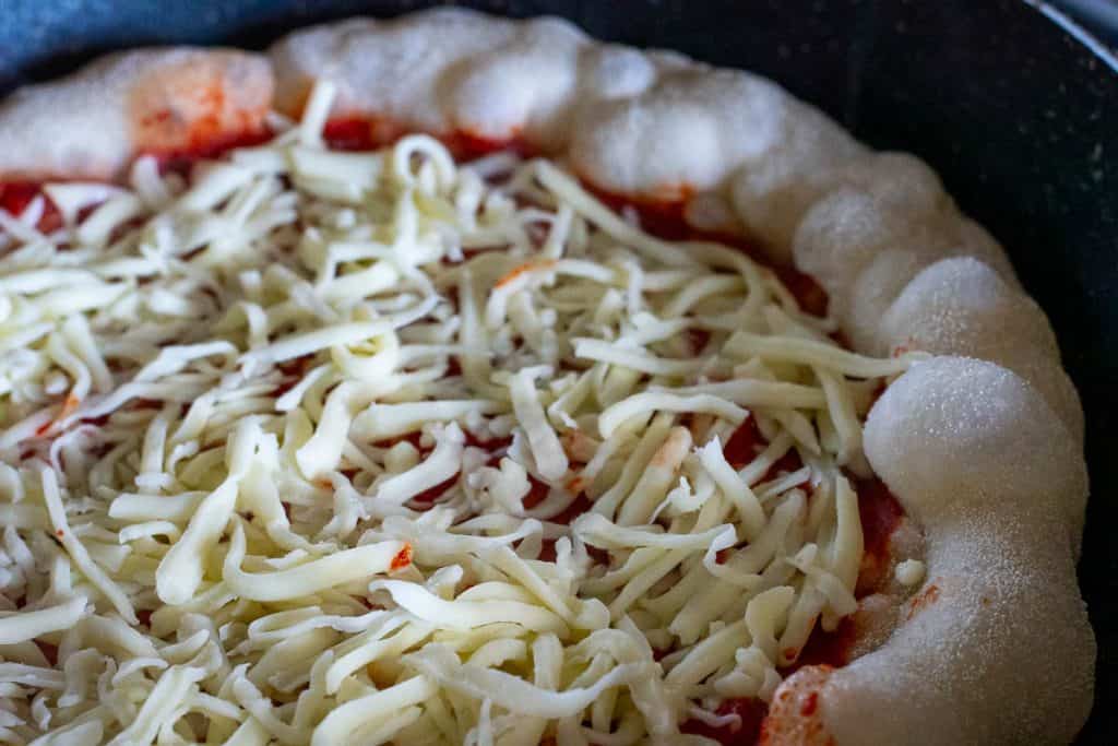 Grated mozzarella spread across the tomato sauce on a sourdough pizza crust.
