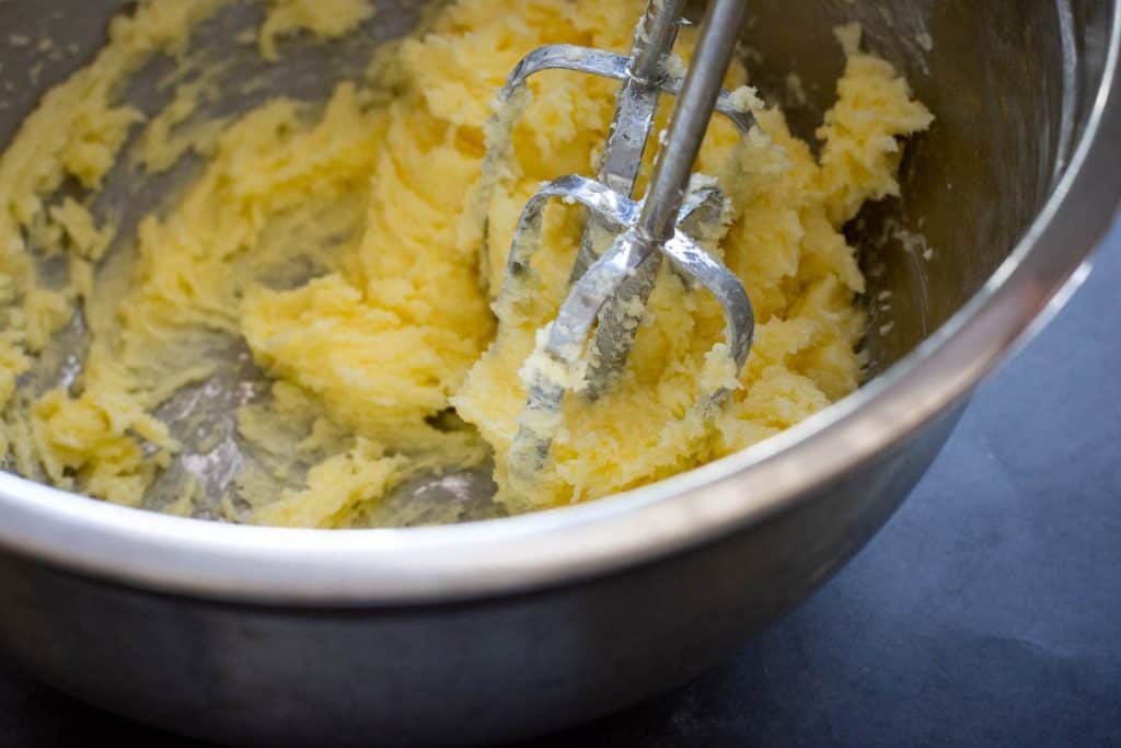 Creaming butter and sugar using an electric handheld mixer.