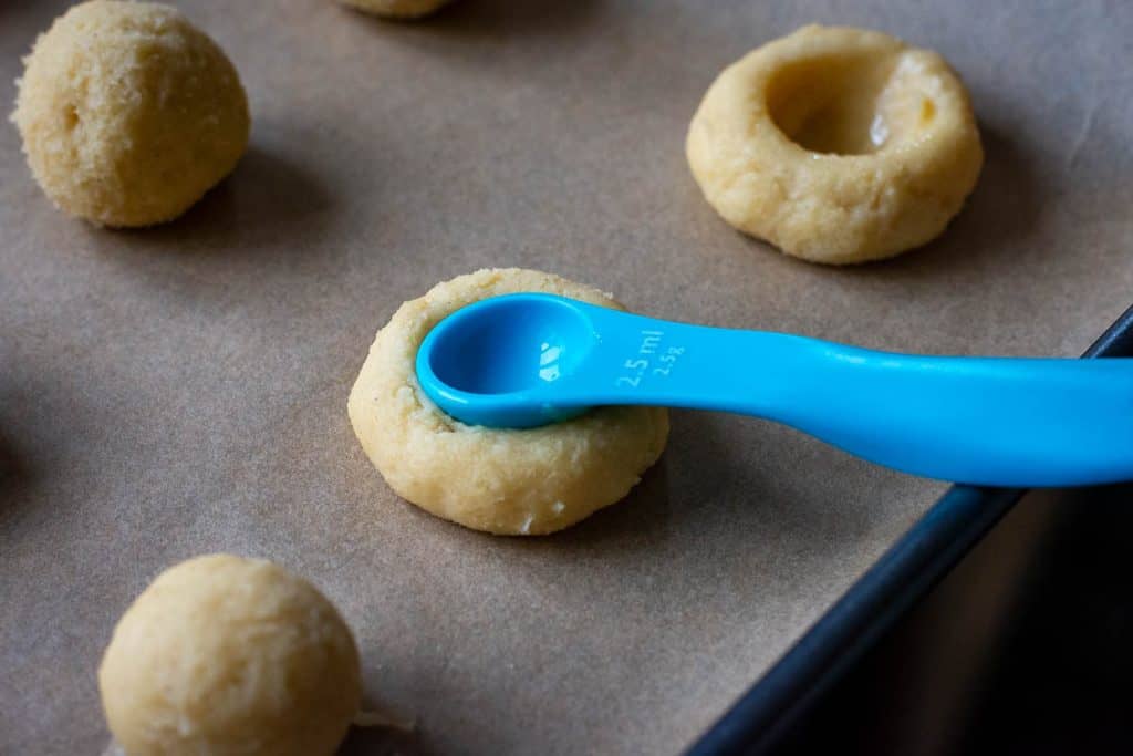Making a dip in the middle of each cookie using a measuring spoon.
