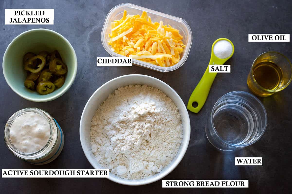 Labelled ingredients for Sourdough Focaccia with Jalapenos and Cheddar on a dark kitchen surface.