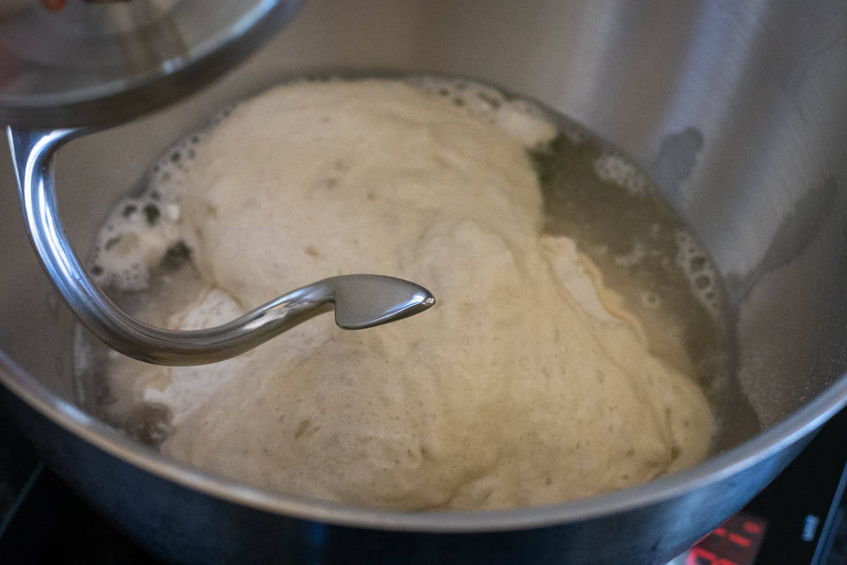 Flour, water and active sourdough starter in a stand mixer bowl with a dough hook attachment.