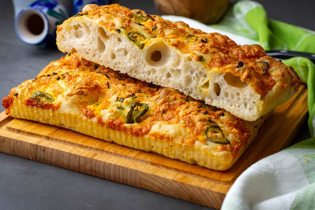 Sourdough focaccia with cheddar and jalapenos sliced into long strips on a wooden board.
