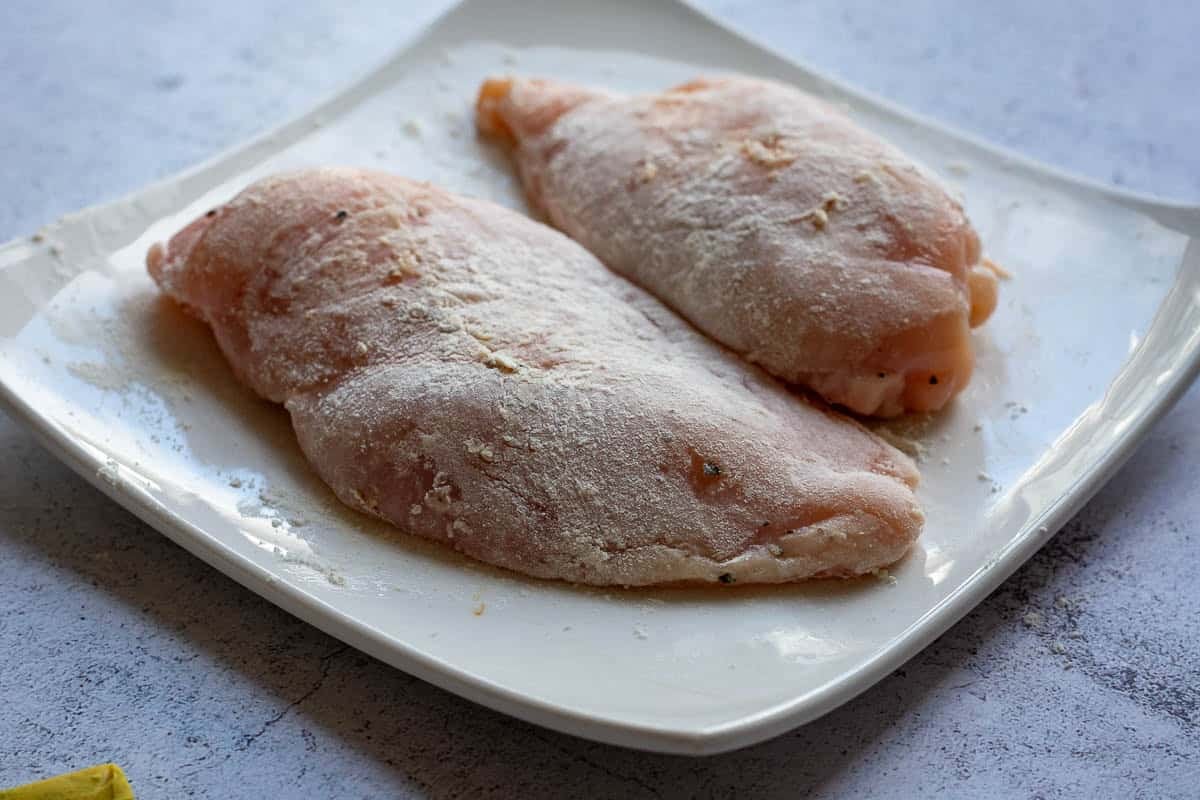 Flour coated chicken breast on a small white plate.