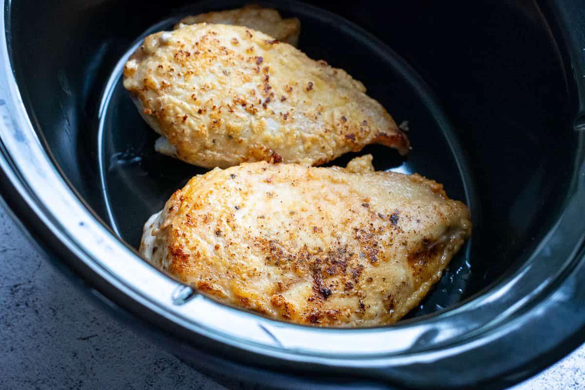 Seared chicken breasts in a bowl of a slow cooker.