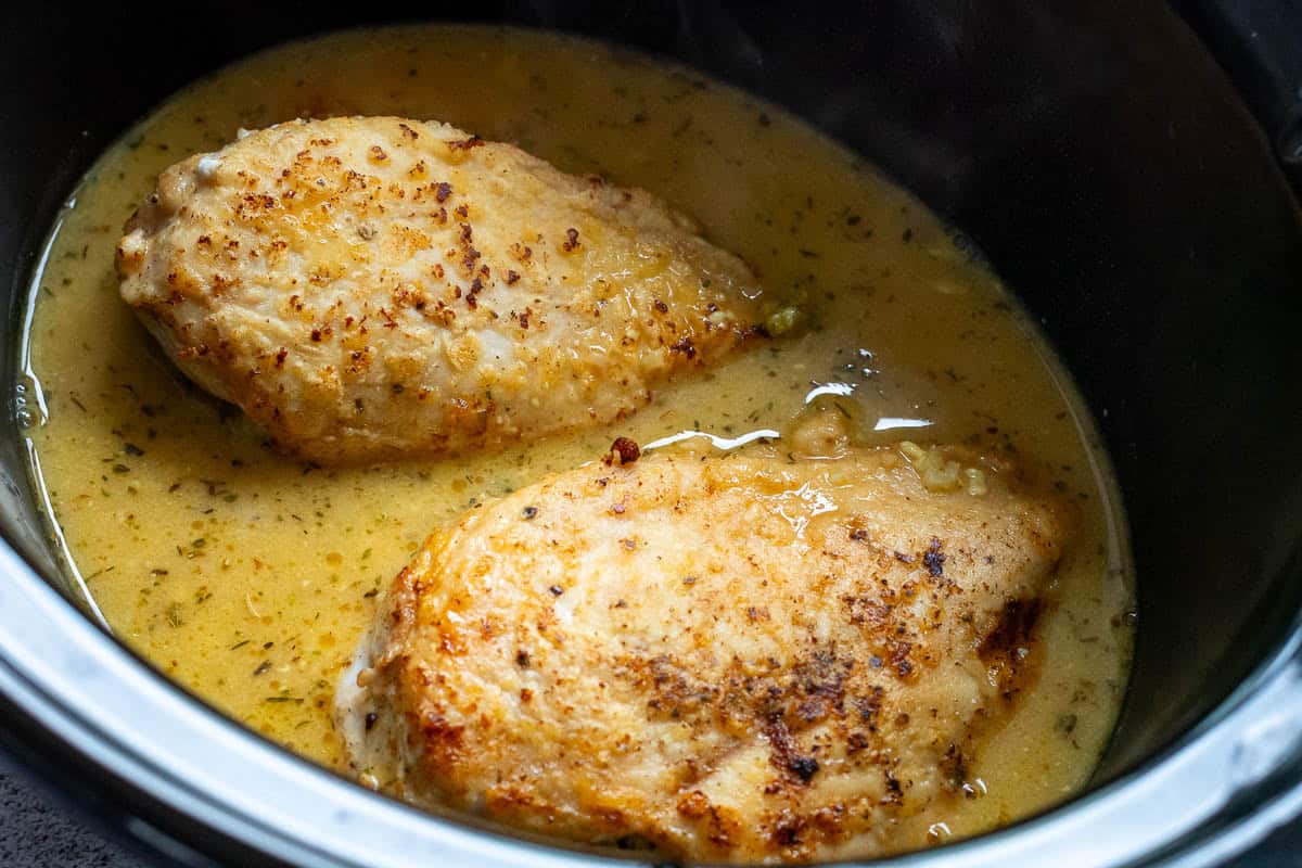Two chicken breasts in honey mustard sauce in a slow cooker bowl.