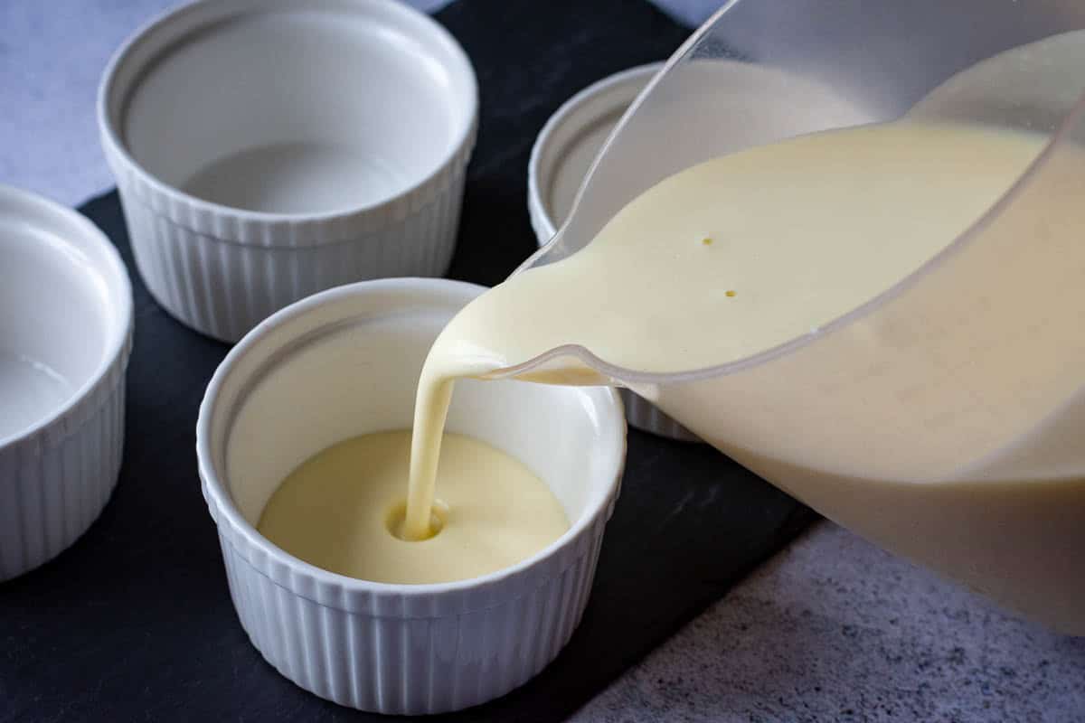 Pouring yuzu panna cotta mixture into white ramekins.