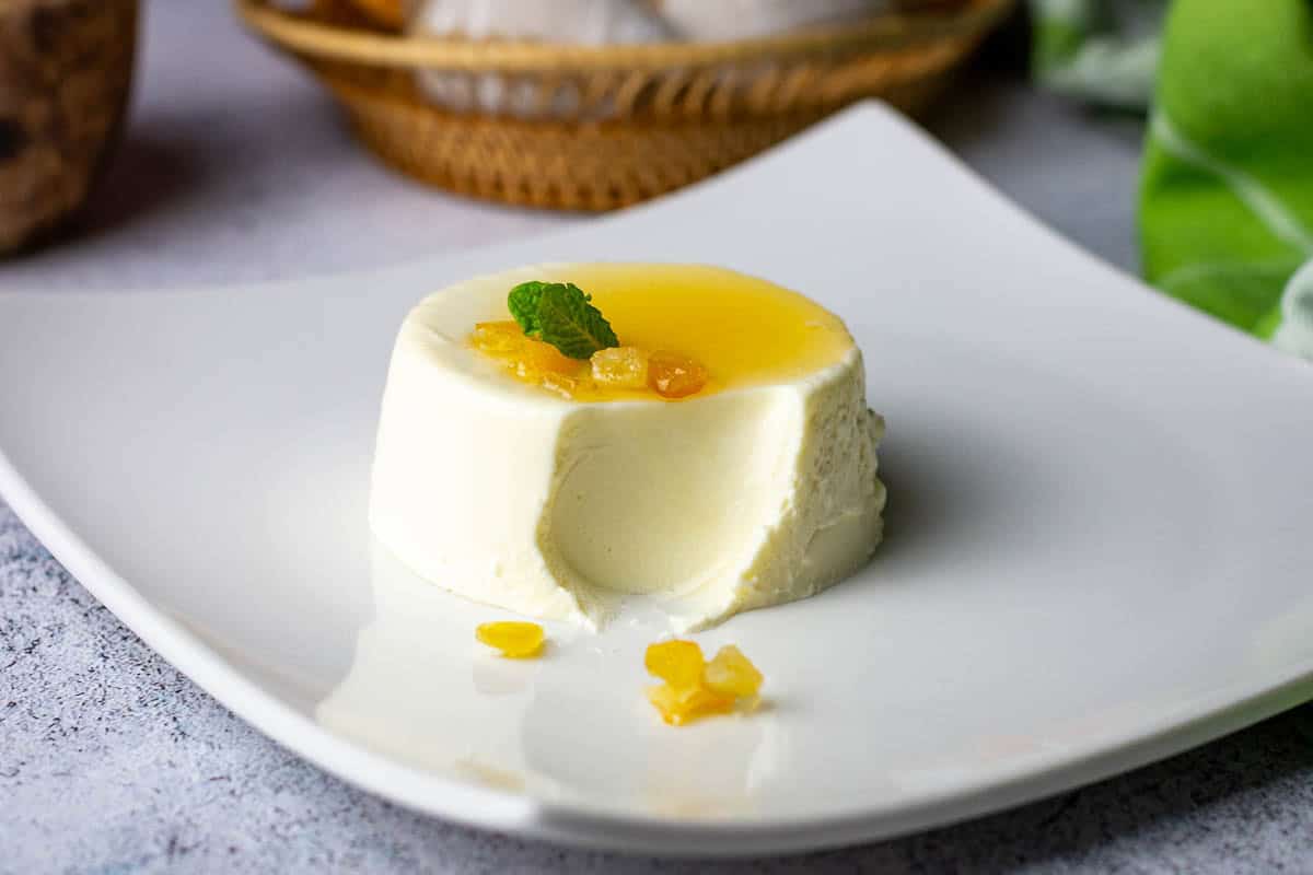 Yuzu panna cotta topped with yuzu syrup and candied peel on a white plate, already missing a spoonful.