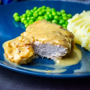 Slow cooker honey mustard chicken breast on a blue plate with mashed potato and green peas.
