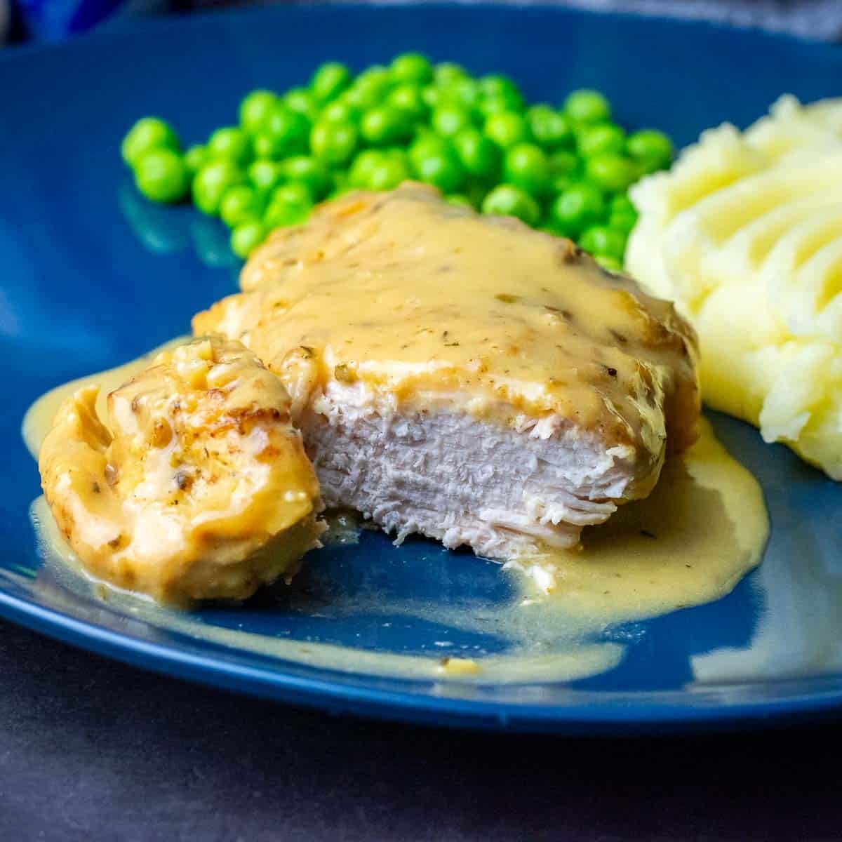Slow cooker honey mustard chicken breast on a blue plate with mashed potato and green peas.