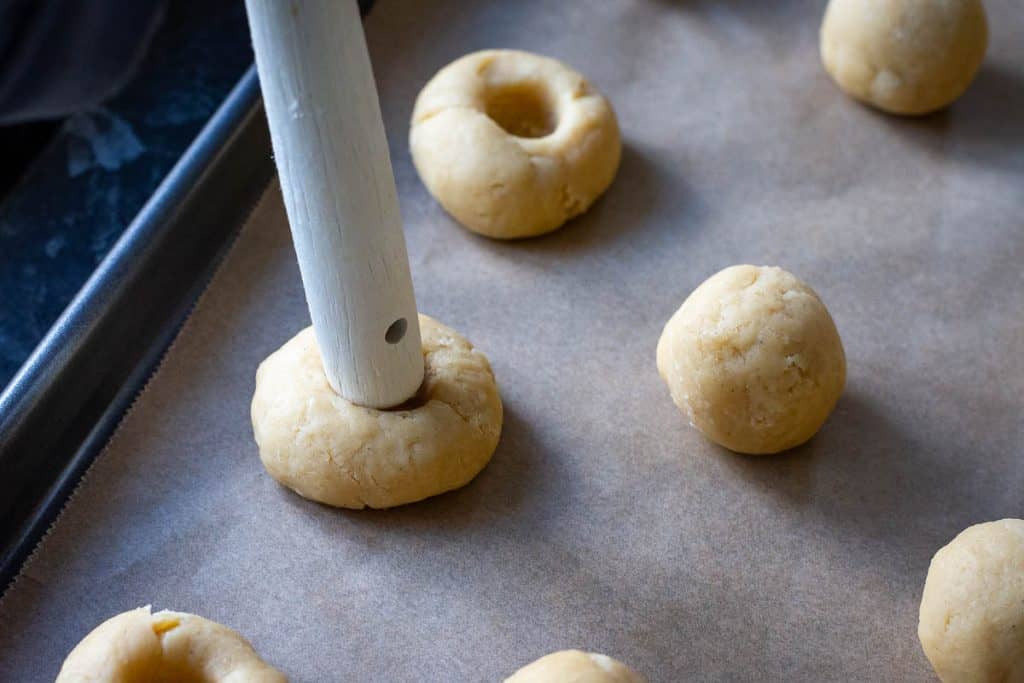 Using a wooden handle of a spatula to create indents in the sourdough cookie balls.