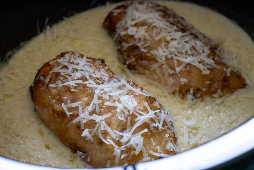 Slow cooked lemon chicken breasts in cream sauce in a slow cooker bowl.