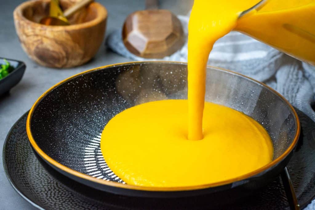 Pouring silky smooth carrot and sweet potato soup into a black bowl.