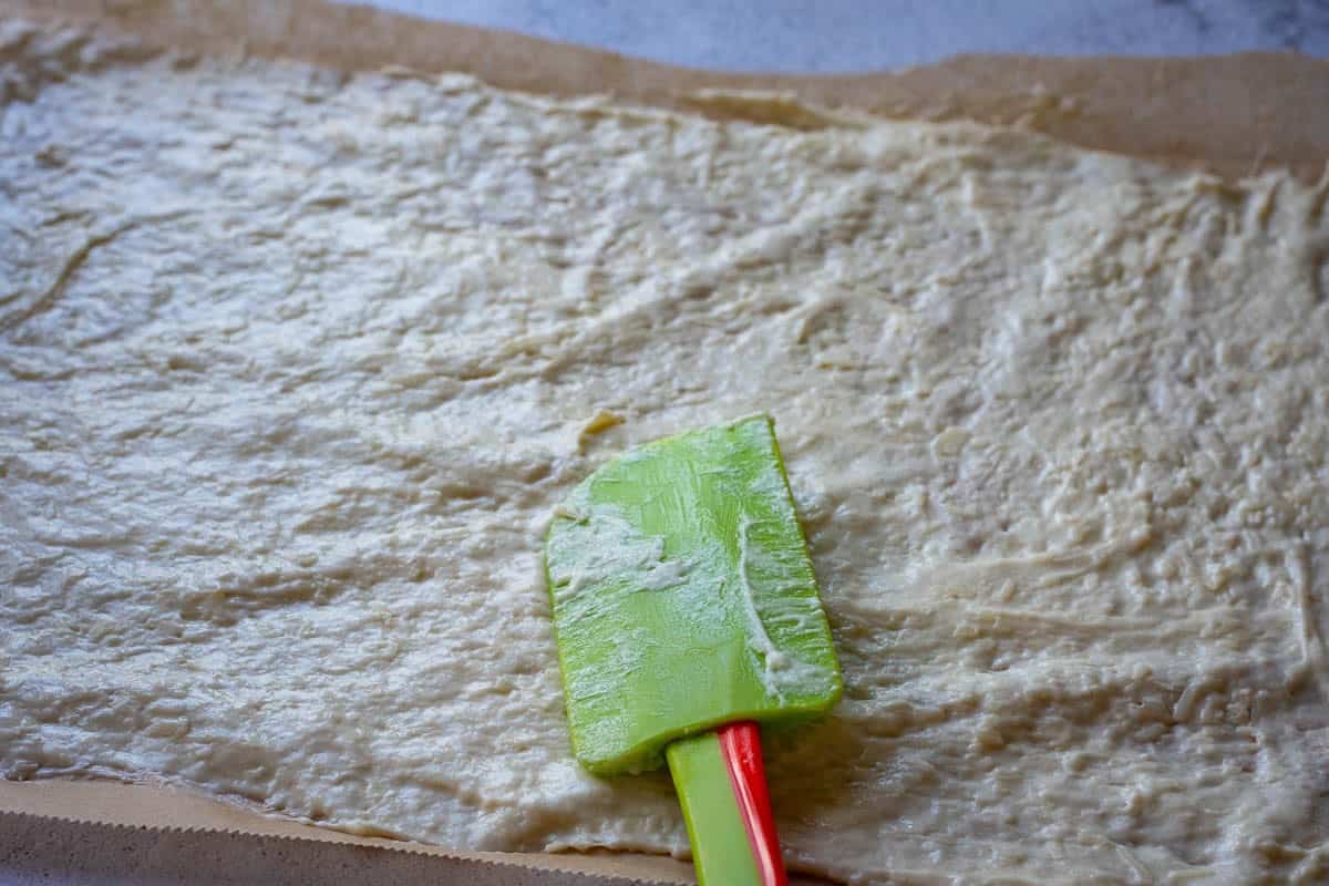 Spreading sourdough discard parmesan cracker mixture thinly on a parchment paper lined baking sheet.