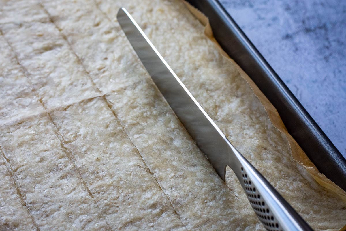 Cutting par-baked sourdough parmesan crackers with a long bladed knife.