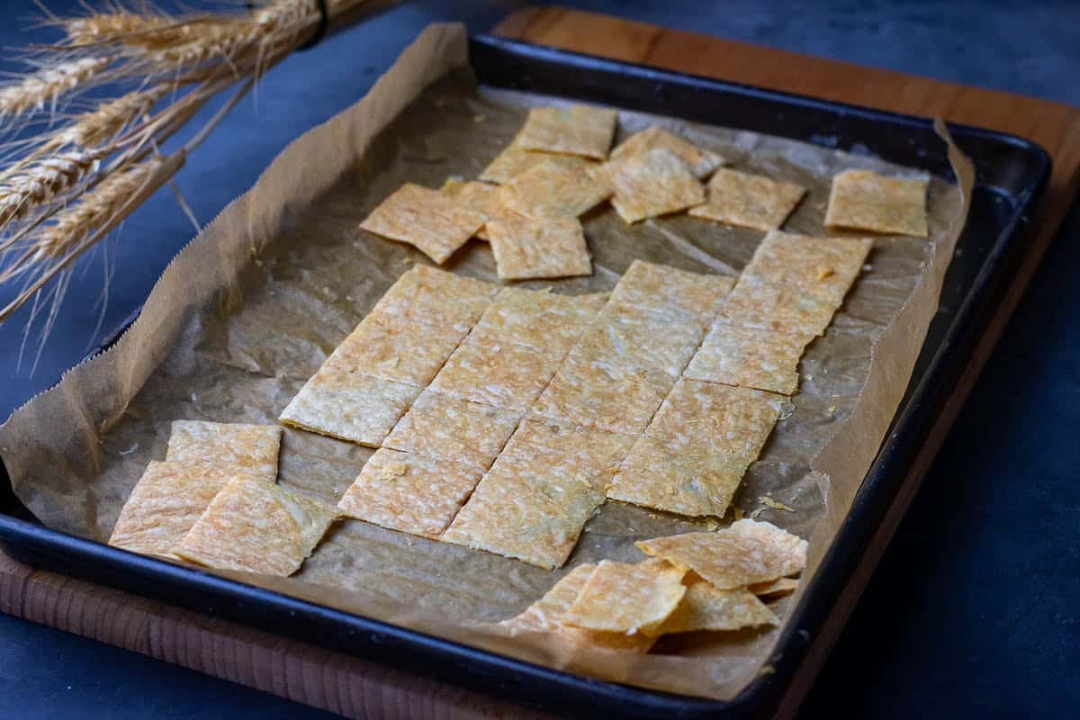 Golden brown parmesan sourdough crackers broken up on a baking sheet.