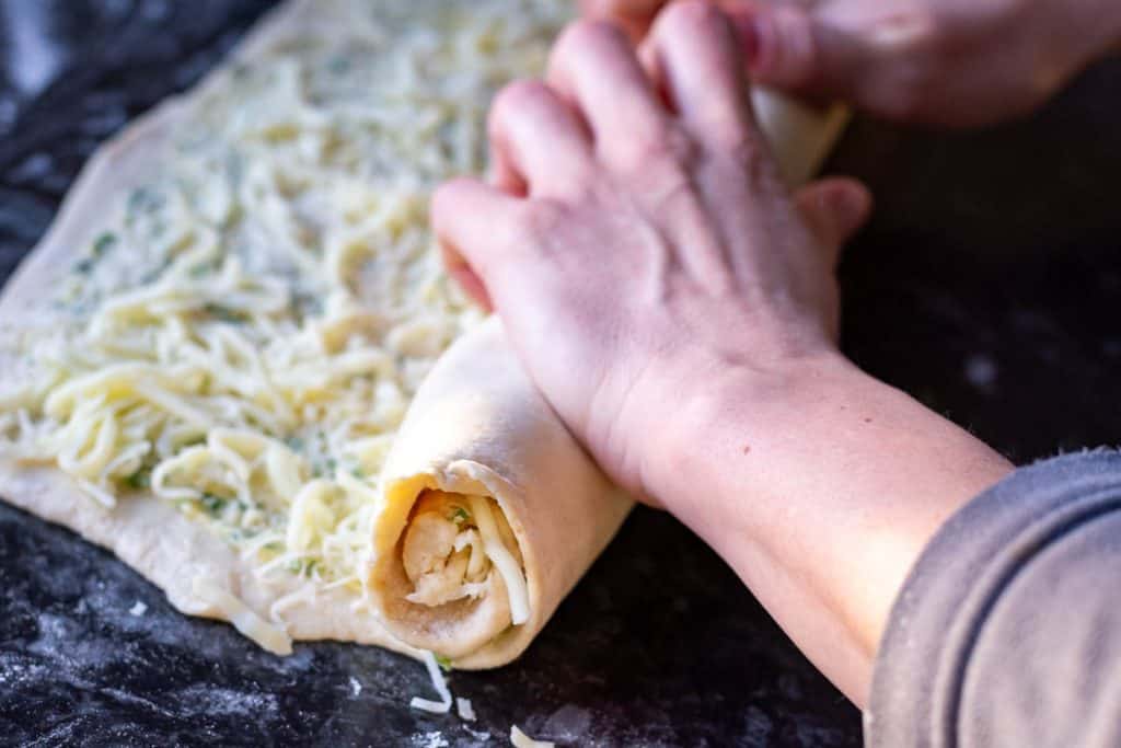 Rolling the sourdough with cheese and garlic butter filling into a tight log.