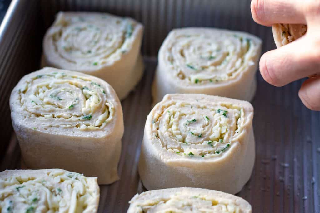 Nine cheese and garlic sourdough rolls being arranged in the baking tray.