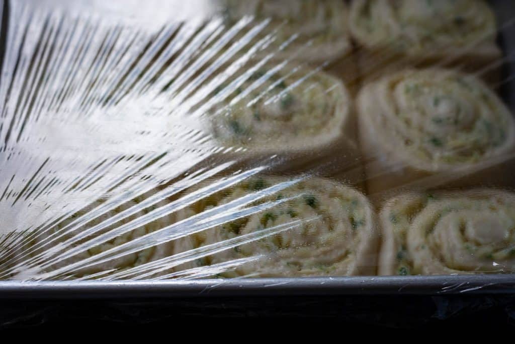 Sourdough Cheese rolls in a baking tray covered with plastic wrap for their second proof.