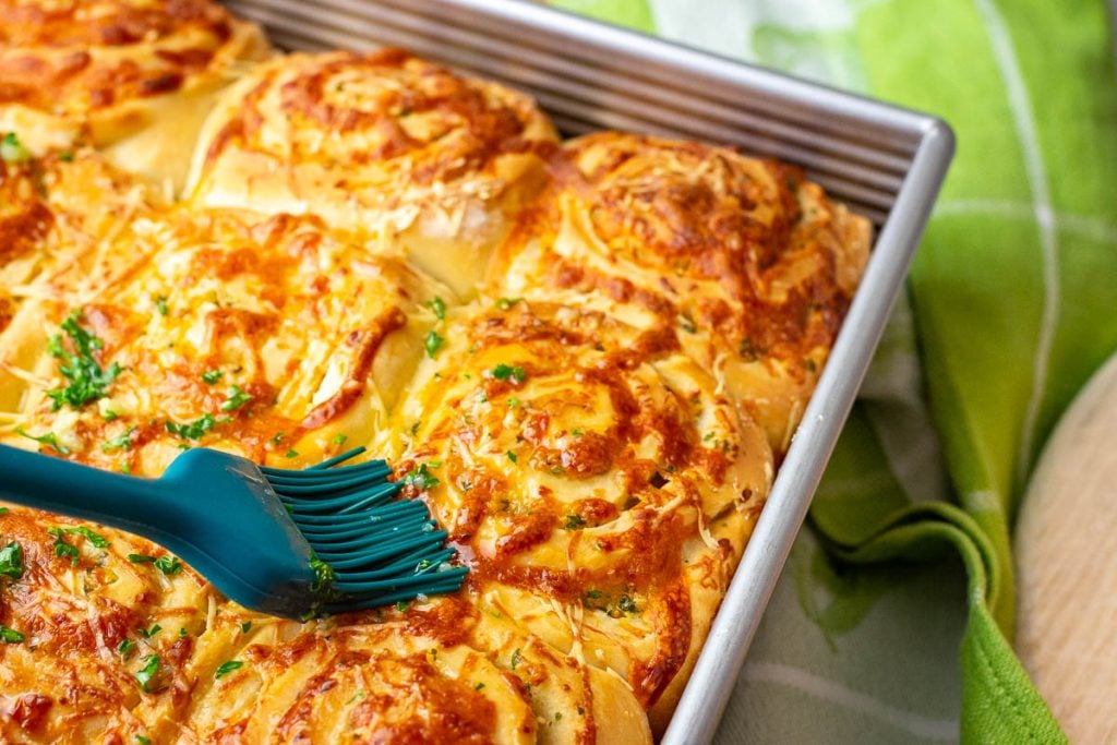 Brushing garlic butter over the baked sourdough cheese rolls.