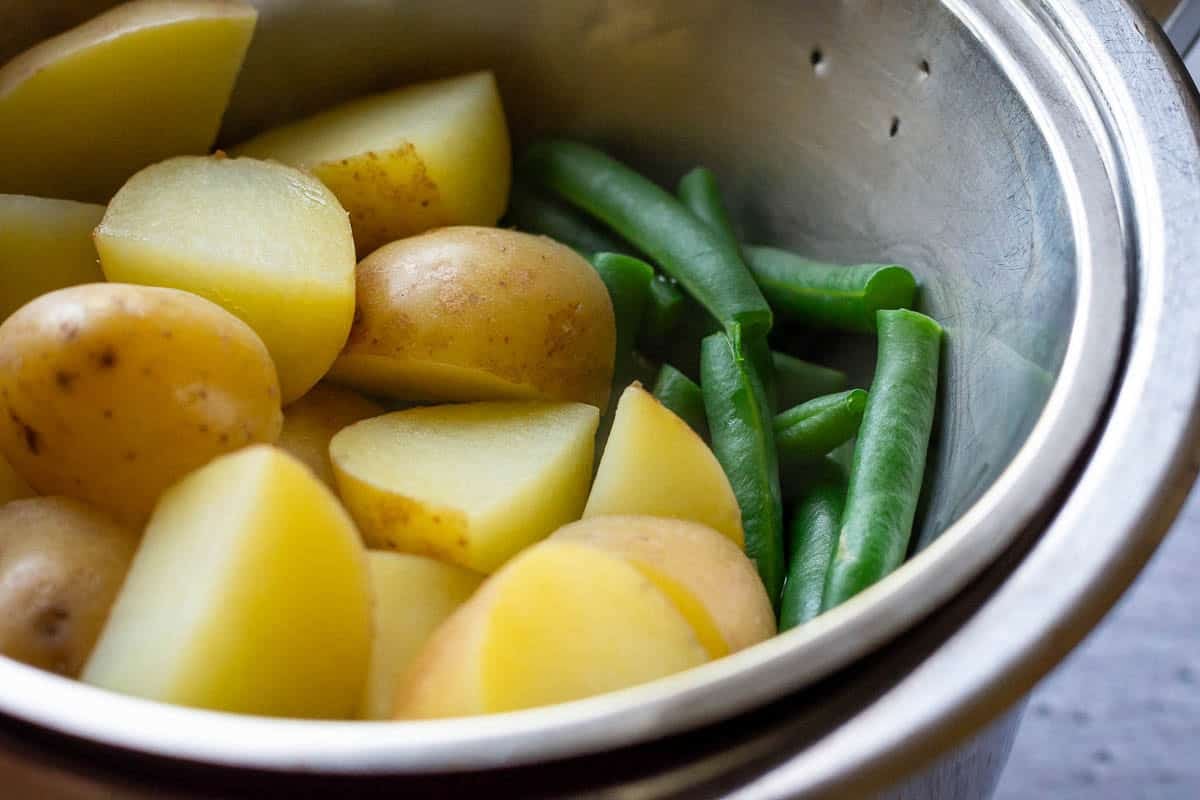 Par-boiled potatoes and green beans in colander.