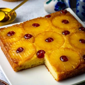 A sourdough pineapple upside down cake on a white plate with one slice already cut.