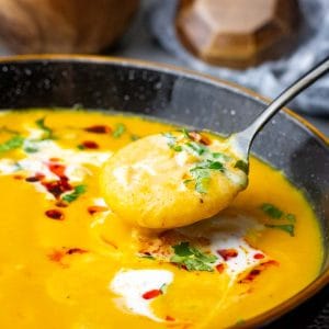Sweet potato and carrot soup made with coconut milk topped with crunchy chilli oil and coriander being eaten with a spoon.