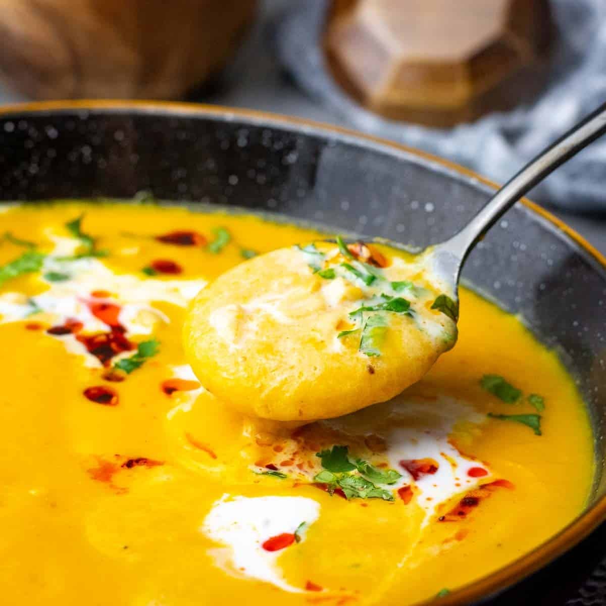 Sweet potato and carrot soup made with coconut milk topped with crunchy chilli oil and coriander being eaten with a spoon.