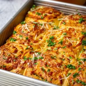 Cheesy Garlic Sourdough Rolls with parsley and garlic butter brushed on top in a square baking pan.