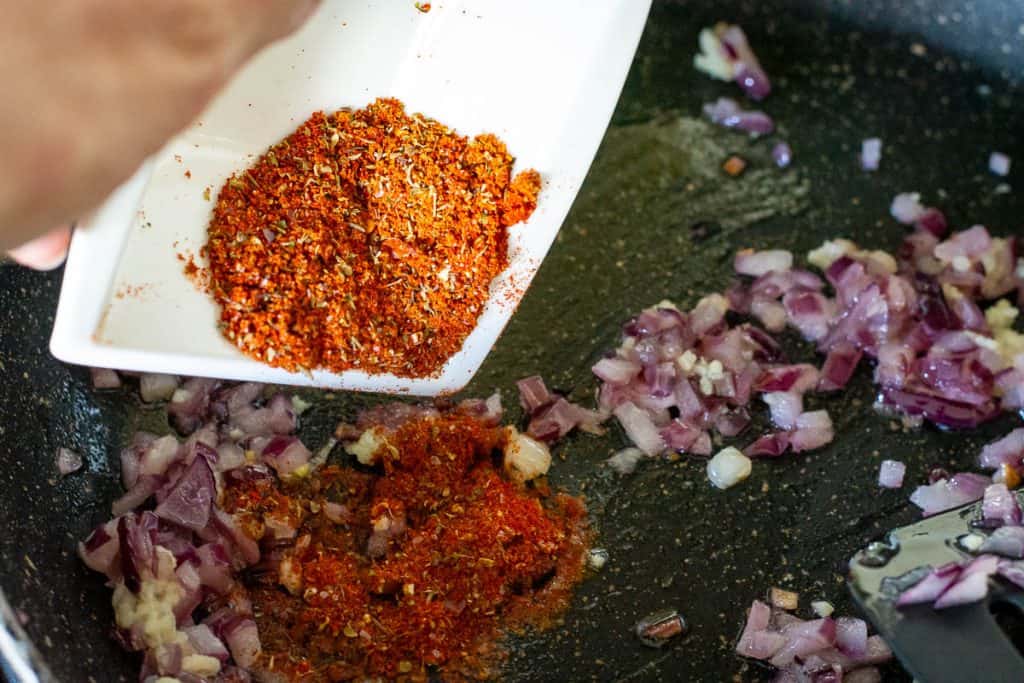 Adding spices into the frying pan with onion.