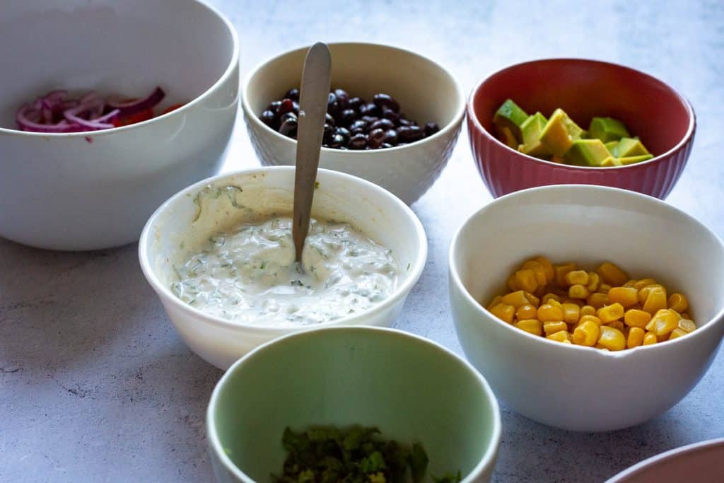 Toppings and sauce for turkey burrito bowls in lots of different small bowls.