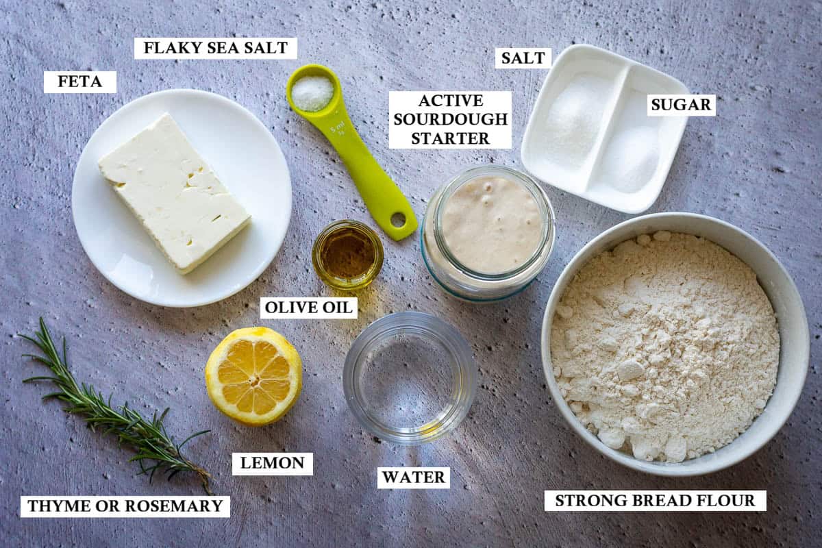 Labelled ingredients for savoury lemon and feta sourdough focaccia on a grey surface.